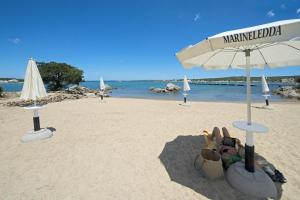 a sandy beach with an umbrella and shoes on it at Marineledda Apartments in Golfo Aranci