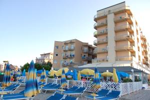 eine Gruppe blauer Stühle und Sonnenschirme vor einem Gebäude in der Unterkunft Bikini Tropicana Family Hotel in Lido di Savio