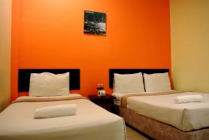 two beds in a room with an orange wall at Wau Hotel & Cafe in Jerantut