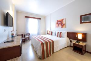 a hotel room with a large bed and a table at Hotel Carlton Plaza in Poços de Caldas