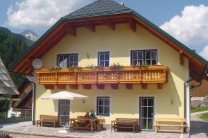 Casa amarilla con balcón de madera y mesas. en Ferienhof Rinnergut, en Hinterstoder