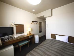 a hotel room with a bed and a desk with a television at Hotel Route-Inn Court Karuizawa in Miyota