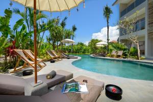 a resort pool with lounge chairs and an umbrella at Canggu Beach Apartments in Canggu