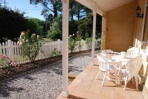 um pátio com cadeiras brancas, uma mesa e uma cerca em Hillside Cottage Berrima em Berrima