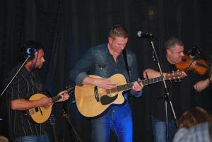 a group of three men playing guitars on a stage at Dolphin Hotel in Inishbofin