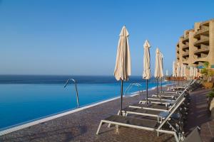 a row of beach chairs with umbrellas and the water at Gloria Palace Royal Hotel & Spa in Puerto Rico de Gran Canaria