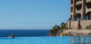 a person in a swimming pool looking at the ocean at Gloria Palace Royal Hotel & Spa in Puerto Rico de Gran Canaria