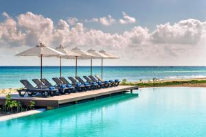 El Beso Adults Only at Ocean Riviera Paradise All Inclusive في بلايا ديل كارمن: صف من الكراسي والمظلات على رصيف مع المحيط