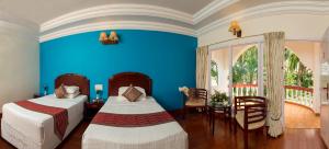 1 dormitorio con 2 camas, mesa y pared azul en GReaT Trails Riverview Thanjavur By GRT Hotels en Thanjāvūr