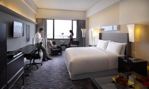 a hotel room with a bed and a man standing at a desk at PARKROYAL Saigon in Ho Chi Minh City