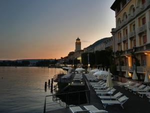 a row of chairs and umbrellas on the water near a building at Grand Hotel Gardone in Gardone Riviera