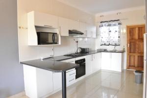 a kitchen with white cabinets and a black counter top at Asante Apartments in Livingstone