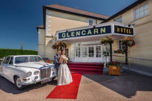 a bride and groom standing in front of a car at The Glencarn Hotel in Castleblayney
