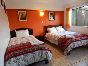 2 camas en una habitación con paredes de color naranja en Hospedaje Qori Punku, en Cusco