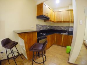 una pequeña cocina con armarios de madera y taburetes. en Golden Gate Suites en Dumaguete