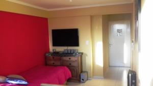 1 dormitorio con 1 cama y TV en una pared roja en Temporario en Villa Sol en Córdoba