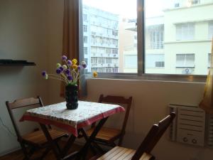 una mesa con un jarrón de flores con una ventana en Apart Marcelo - Copacabana, en Río de Janeiro