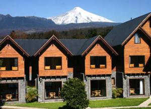 a large wooden house with a snow covered mountain in the background at Alpes Hotel in Pucón