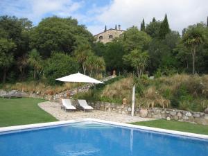 a pool with an umbrella and chairs and a building at Can Serola in Sales del Llierca