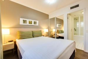 a bedroom with a large white bed and a mirror at Oakbridge Hotel & Apartments Brisbane in Brisbane