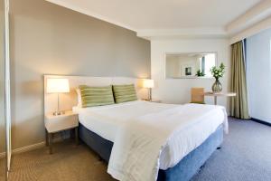 a bedroom with a large white bed and a mirror at Oakbridge Hotel & Apartments Brisbane in Brisbane
