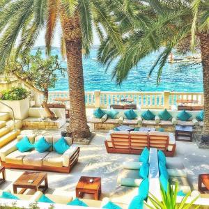 a resort patio with couches and palm trees and the ocean at HVAR apartments 8 min to the beach in Hvar