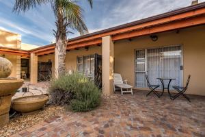 une terrasse avec une table, des chaises et un palmier dans l'établissement Guesthouse De Tijger Lodge, à Parow