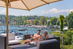 a man and woman sitting on a patio with a glass of wine at Seehotel Hubertushof in Velden am Wörthersee