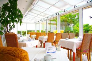 un restaurante con mesas y sillas blancas y ventanas en Hotel Flörke, en Langeoog