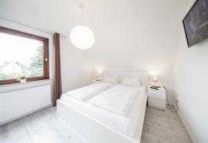 a white bedroom with a white bed and a window at Dünenhaus Steinmarne in Cuxhaven