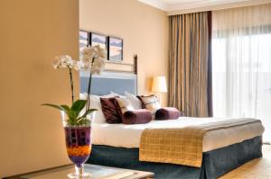 a bedroom with a bed and a vase with flowers on a table at Corinthia St George's Bay in St. Julianʼs