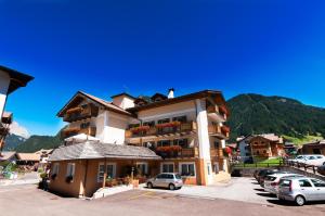 un grand bâtiment avec des voitures garées dans un parking dans l'établissement Hotel El Geiger, à Pozza di Fassa