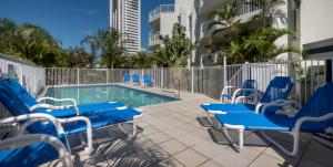 a swimming pool with blue chairs next to a building at Santa Anne By The Sea in Gold Coast