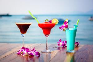 three cocktails and flowers on a table near the ocean at Secret Garden Beach Resort in Bangrak Beach