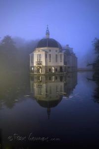 uma casa sobre a água com o seu reflexo na água em de zanderij em 's-Graveland