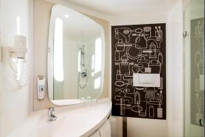 La salle de bains est pourvue d'un miroir et d'un lavabo blanc. dans l'établissement Ibis Schiphol Amsterdam Airport, à Badhoevedorp