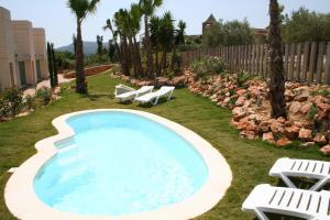 a swimming pool with two lawn chairs and two white chairs at L' Escala Resort in L'Escala