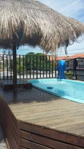 a swimming pool with a straw umbrella on a deck at Suítes Tropicana guesthouse in Cabo Frio