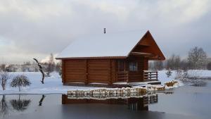 a log cabin in the snow next to a body of water at Lindiki in Salaspils