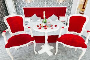 una mesa blanca con 2 sillas rojas y una botella de vino en Pensiunea Avy, en Haţeg