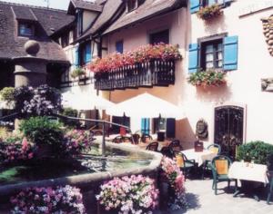 um pátio com mesas e cadeiras e um edifício com flores em Auberge du Rempart em Eguisheim