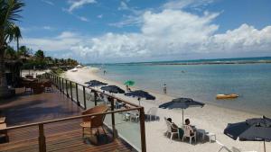 a beach with umbrellas and people sitting on the sand at Muro Alto Marupiara Flats in Porto De Galinhas