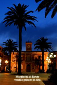 a building with a clock tower and palm trees at night at Casa Geranio in Margherita di Savoia