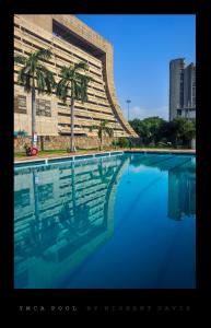 a swimming pool with palm trees in front of a building at New Delhi YMCA Tourist Hostel in New Delhi