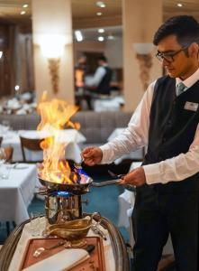 a man holding a utensil in front of a grill with flames at Thermal Hotels & Walliser Alpentherme Leukerbad in Leukerbad