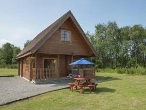 a wooden cabin with a picnic table and a blue umbrella at Benview Lodges in Kepculloch