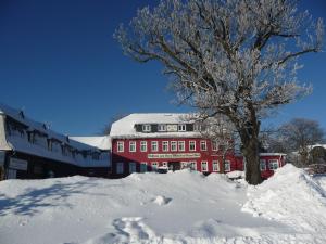 ein rotes Gebäude mit einem Baum im Schnee in der Unterkunft Zum Roten Hirsch im Grünen Wald in Saalfeld