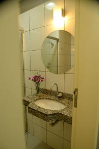 a bathroom sink with a mirror and a vase of flowers at Hotel Calypso in Nova Serrana