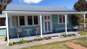 Mapua的住宿－Ferntree Cottage，蓝色的房子,门廊上设有两把椅子和一张桌子
