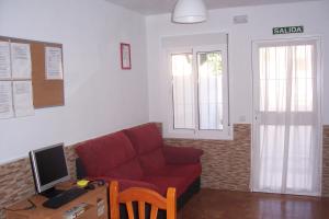 a living room with a red couch and a desk with a computer at Pensión Nomphosumus in Cala del Moral